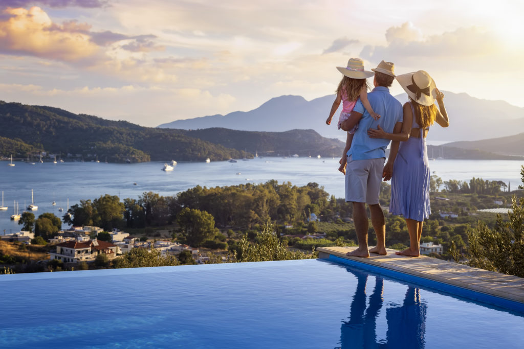 A family on summer holidays stands by the swimming pool and enjoys the beautiful sunset